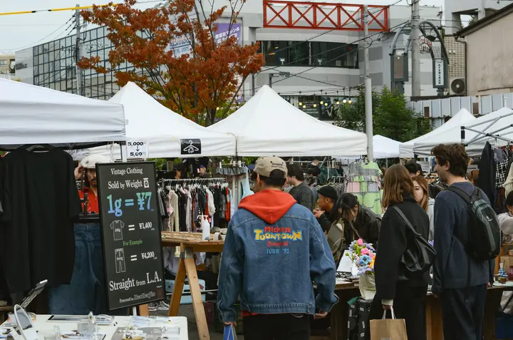 「1g = ¥7」と書かれた量り売りの看板が出た古着ブースと、品定めをする来場者