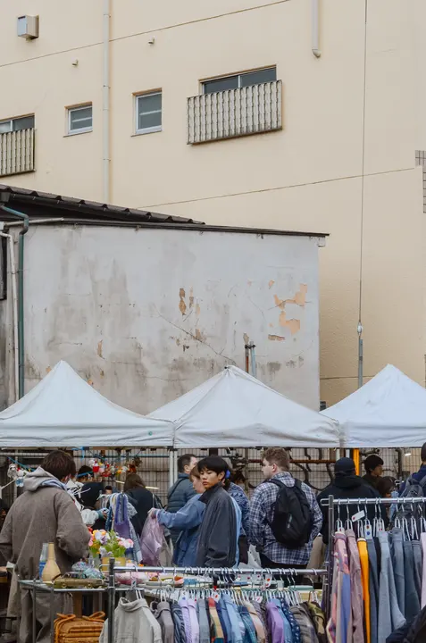 白い壁の建物の前に張られた三つのテントと、古着のラックを見る来場者