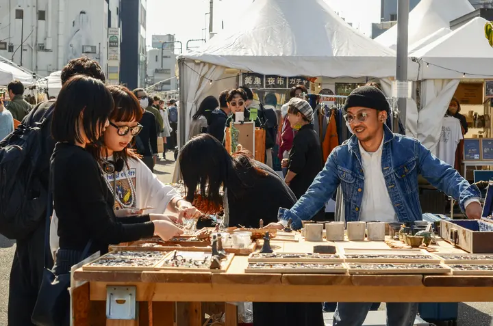 木の台にずらりと並んだ小物を、出店者と来場者が挟んで見ている様子