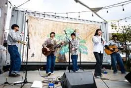 屋外ステージでアコースティック演奏をする出演者と、見に集まった人たち