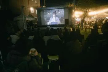夜の屋外で行われる映画上映と、それを見る来場者